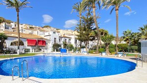 A swimming pool with a tiled deck, surrounded by palm trees and buildings with white facades and red awnings. - Villa Seaview Punta Lara by Casasol (Nerja)