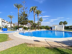 A swimming pool with a tiled deck, surrounded by palm trees and a clear blue sky. - Villa Seaview Punta Lara by Casasol (Nerja)