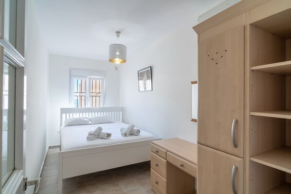 A bedroom with a bed, a wooden wardrobe, a desk, and a hanging light fixture.