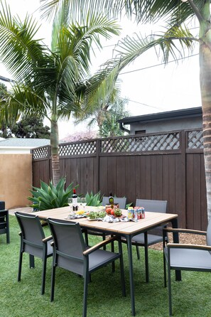 Eine Terrasse im Freien mit einem Holztisch und -stühlen, umgeben von Palmen und einem Holzzaun.