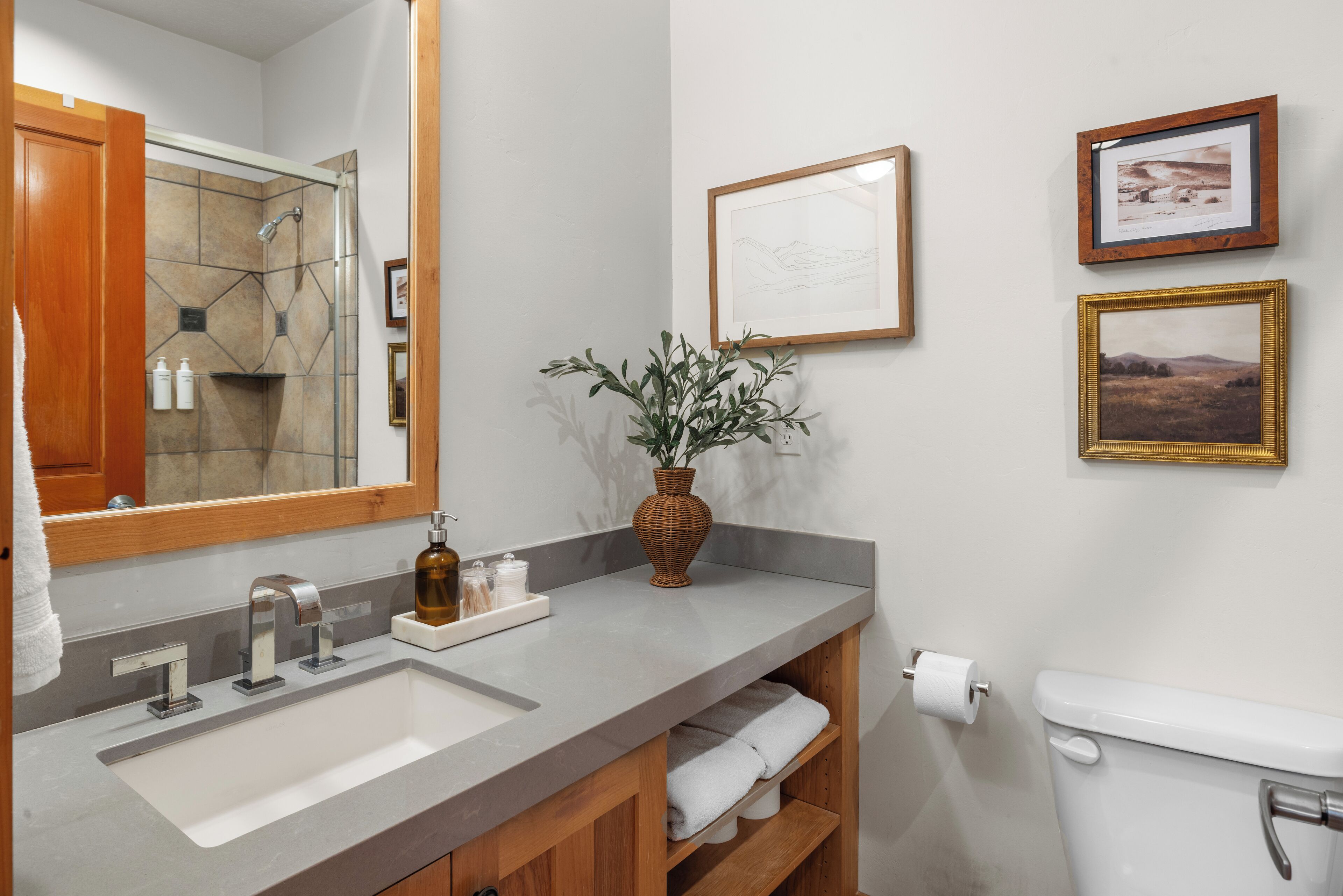 A bathroom with a large mirror, a sink, a toilet, and a shelf with towels.