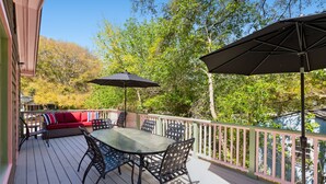 Une terrasse en bois avec une table et des chaises, un canapé rouge et deux parasols.