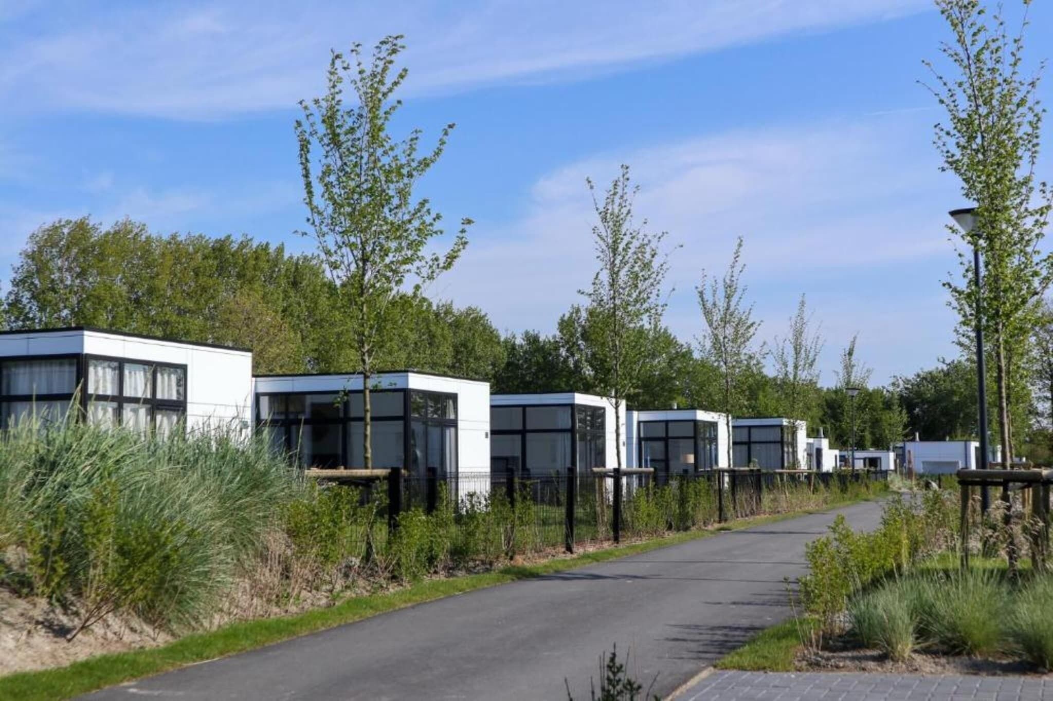 A row of modern, white, boxy buildings with large windows, surrounded by greenery and a paved path.