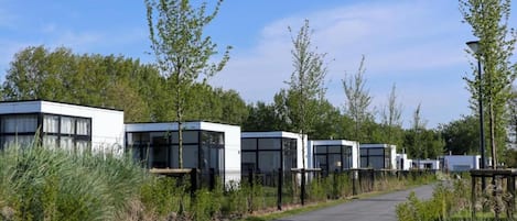 A row of modern, white, boxy buildings with large windows, surrounded by greenery and a paved path.
