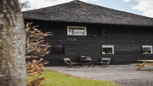 A rustic wooden building with a thatched roof, a small window, and a table with chairs outside.