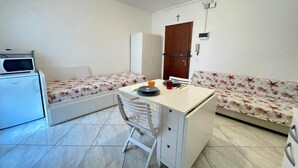 Ein kleines, sauberes Zimmer mit Bett, Schreibtisch, Stuhl, Kleiderschrank und einer Mikrowelle.