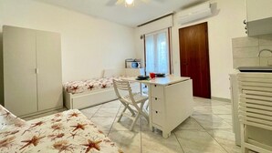 Ein kleines Zimmer mit Bett, Schreibtisch, Stuhl, Deckenventilator und Fenster.