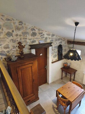 A room with a stone wall, wooden cabinet, table, chairs, and a hanging light fixture.