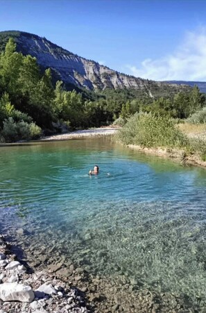 Un río cristalino con una persona nadando, rodeado de terreno rocoso y vegetación.