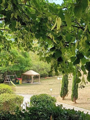 Un parque con zona de juegos, área de descanso cubierta y setos bien recortados.