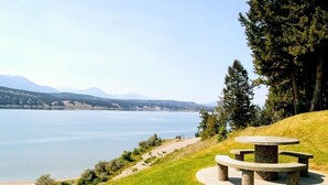 A lakeside view with a circular stone table and benches, surrounded by grass and trees. - Lakeside 3 bed townhome w/ private beach access! (Windermere)