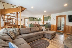 A modern living room with a sectional sofa, wooden staircase, and a kitchen in the background. - Robyn`s Nest - Air Conditioning and Hot Tub! (Davis)