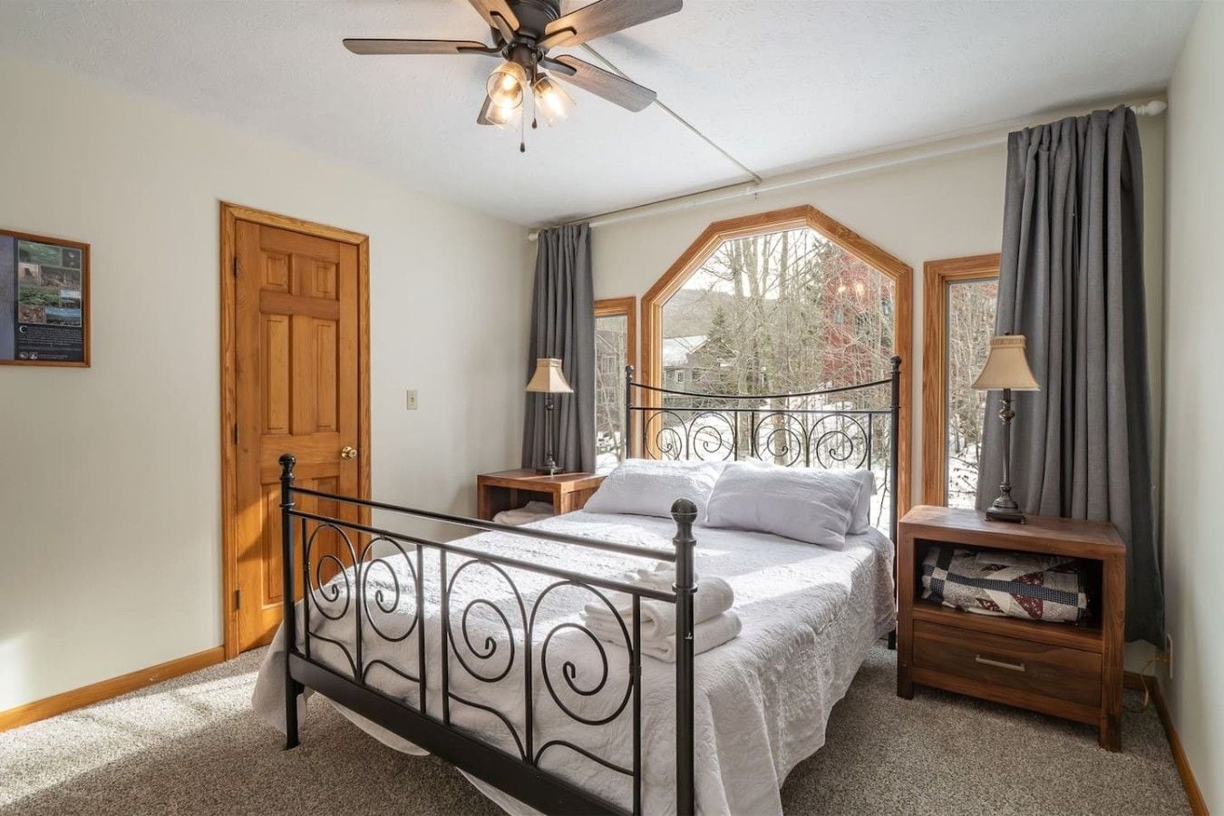 Un dormitorio con cama, ventilador de techo, ventana con cortinas y puerta de madera.