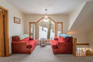 A room with two red sofas, a small round table, and a large window with a view of a snowy landscape. - Robyn`s Nest - Air Conditioning and Hot Tub! (Davis)