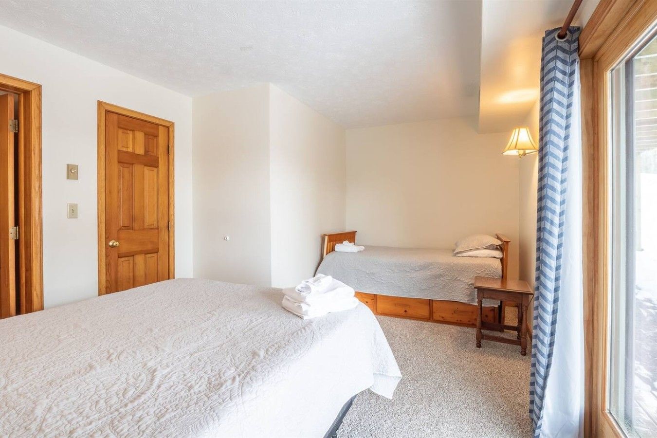 A bedroom with two single beds, wooden doors, and a window with curtains.