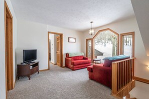 Ein Zimmer mit Fernseher, einem roten Sofa und Blick auf eine verschneite Landschaft durch große Fenster.