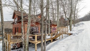 Una cabana de fusta amb terrassa, envoltada d'arbres i un paisatge nevà.