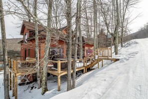 A wooden cabin with a deck, surrounded by trees and a snowy landscape.