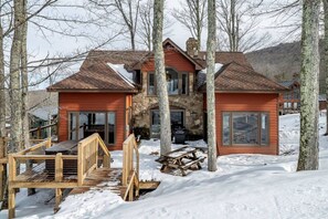 A two-story wooden cabin with a stone chimney, surrounded by snow and trees. - Robyn`s Nest - Air Conditioning and Hot Tub! (Davis)