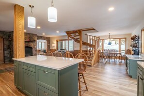 A spacious kitchen with a large island, wooden chairs, and a stone fireplace.