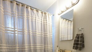 Ein Badezimmer mit Duschvorhang, Waschbecken, Spiegel, Handtuchhalter und Toilette.