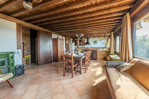 Una cocina rústica con vigas de madera, una zona de comedor con mesa y sillas, y un sofá junto a una ventana.