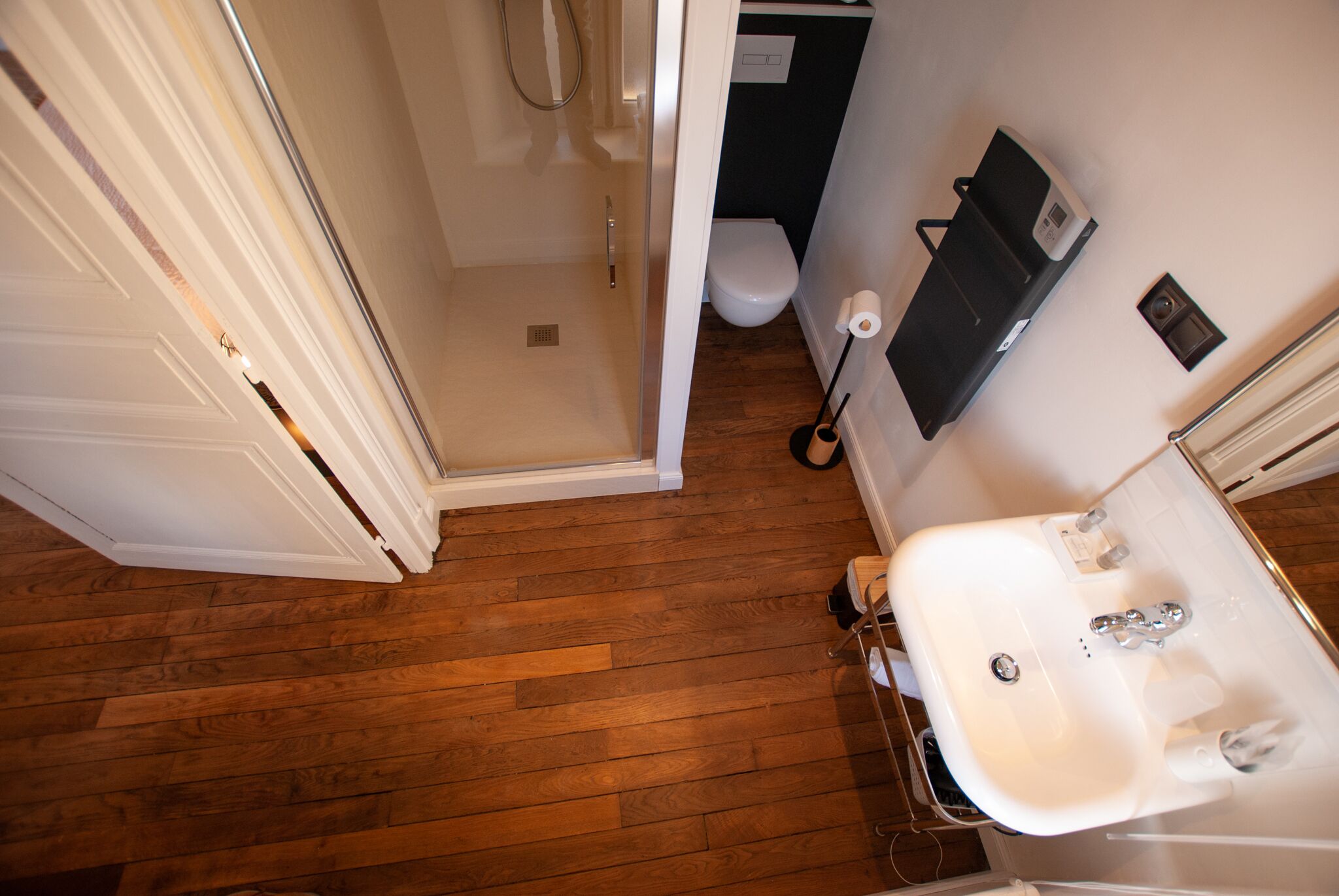 A bathroom with a wooden floor, a white sink, a toilet, and a shower area.