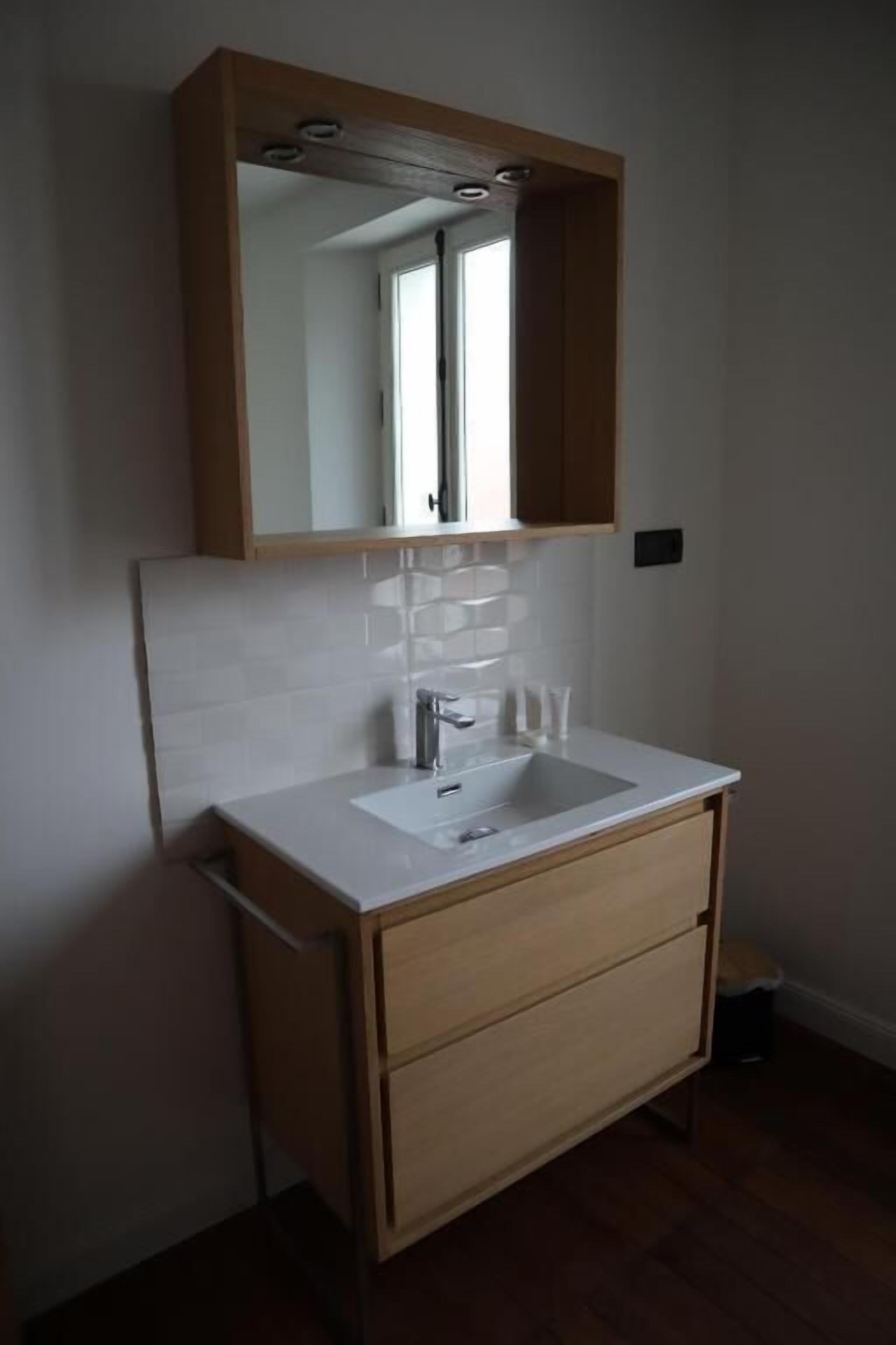 A bathroom with a white sink, wooden cabinet, and a mirror above the sink.