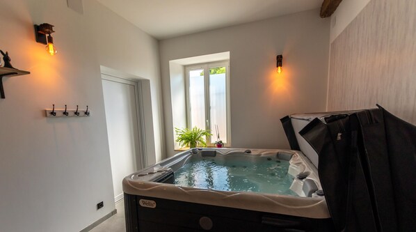 Un jacuzzi en una habitación con ventana, una lámpara de pared y una planta.