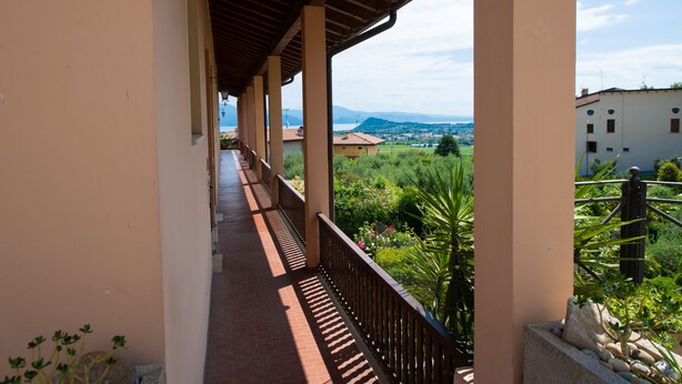 Un balcon fermé offrant une vue sur un paysage verdoyant et des bâtiments éloignés.