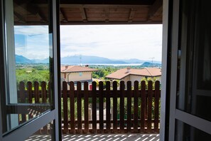 A balcony with a wooden fence, a view of a town with buildings and mountains in the distance. - LakeView (Polpenazze del Garda)