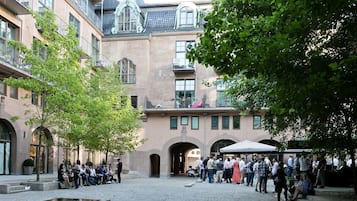 A courtyard with a fountain, surrounded by multi-story buildings with balconies and arched doorways.