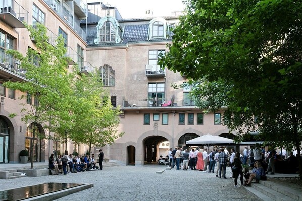 A courtyard with a fountain, surrounded by multi-story buildings with balconies and arched doorways.