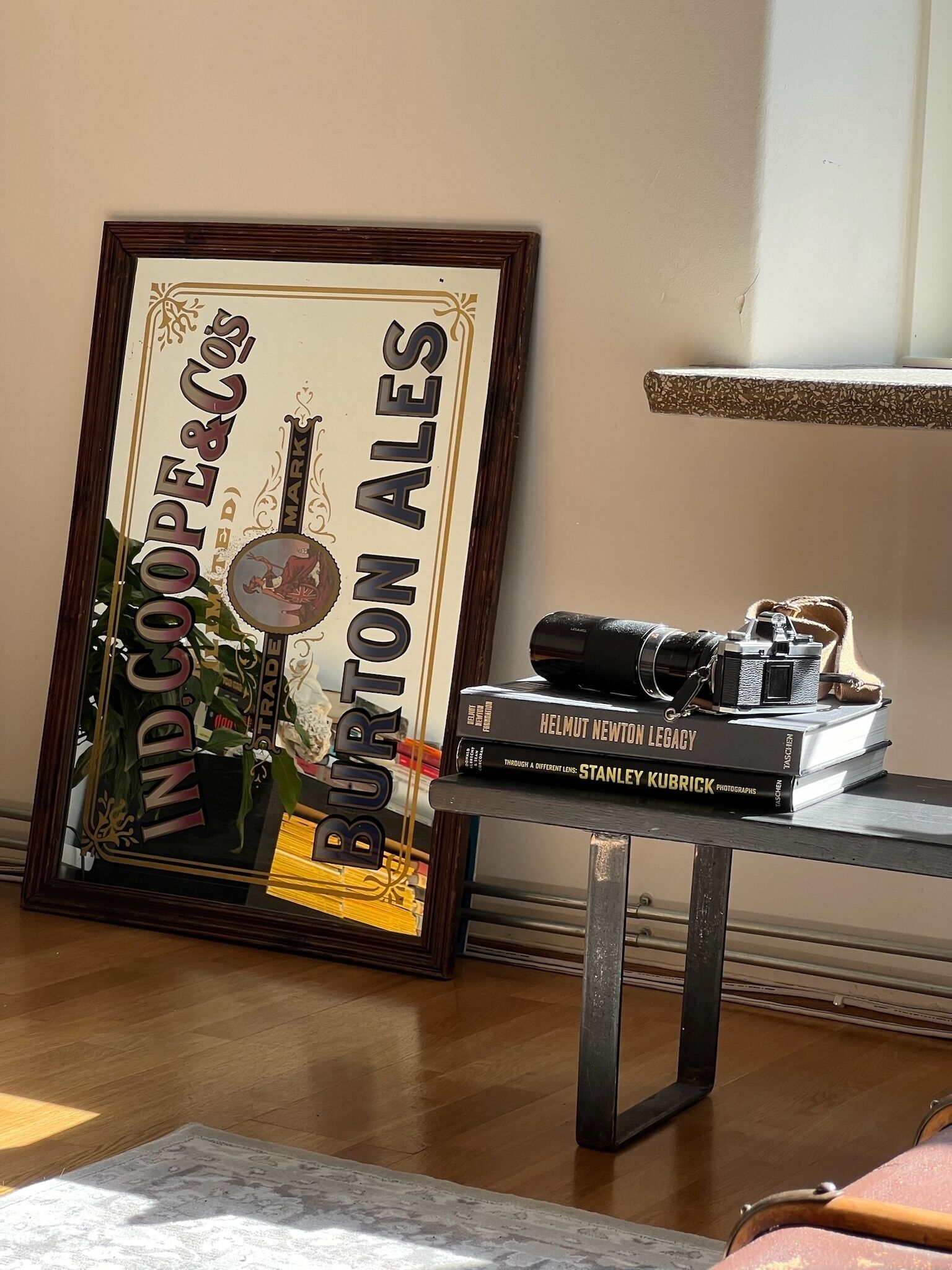 A framed sign with 'IndCooper & Burton Ales' text, a camera, and books on a table.