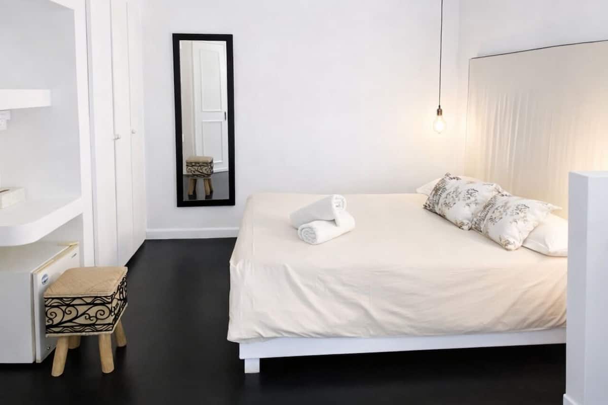 Une chambre à coucher comprenant un lit, un ventilateur de plafond, une lampe de chevet, un miroir et un petit tabouret.