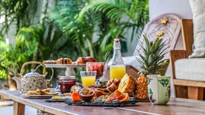 A breakfast table with tropical fruits, pastries, and beverages, set against a backdrop of lush greenery. - Sous le Badamier Boutique Hotel & Spa (Grand-Baie)