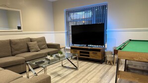 Una sala de estar moderna con un sofá, una mesa de centro de vidrio, un televisor de pantalla plana y una mesa de billar.