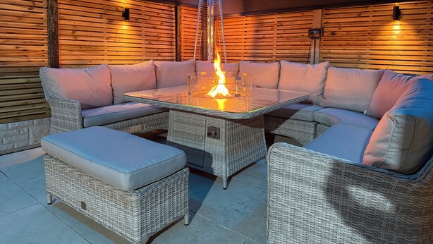 Un espacio exterior acogedor con una mesa de vidrio y una chimenea, rodeado de mobiliario de mimbre y paneles de madera.