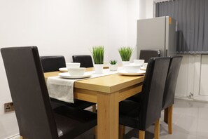 A dining area with a wooden table, black chairs, white plates, and green plants.