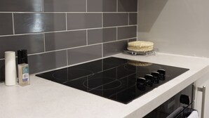 Una cocina con tope de inducción negro, encimera blanca y salpicadero de baldosas grises.