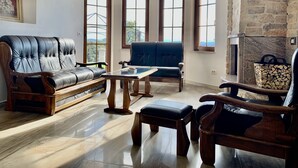 Een woonkamer met een leren bank, een blauwe fauteuil, een houten salontafel en een stenen open haard.