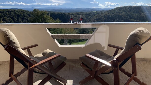 Een terras met twee houten stoelen en een tafel, met uitzicht op een mooi landschap met heuvels en bomen.