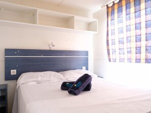 A hotel room with a bed, a headboard, a nightstand, and a window with a plaid curtain.