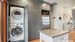 A modern kitchen with a built-in washer and dryer, a stainless steel refrigerator, and a wooden dining table.