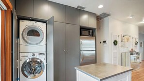 A modern kitchen with a built-in washer and dryer, a stainless steel refrigerator, and a wooden dining table. - Shoal Crest xxxxxxxx (Austin)