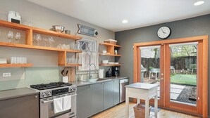 A modern kitchen with stainless steel appliances, wooden shelves, and a dining area with a view of the backyard.