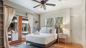 A modern bedroom with a large bed, a ceiling fan, a nightstand, and a window with a view.