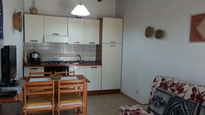 A compact living space with a kitchenette, a dining area with wooden furniture, and a sofa with a floral pattern. - Agriturismo La Barca In Secca (Olmedo)