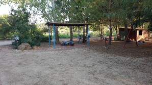 A covered picnic area with benches and a swing set in a wooded park. - Agriturismo La Barca In Secca (Olmedo)