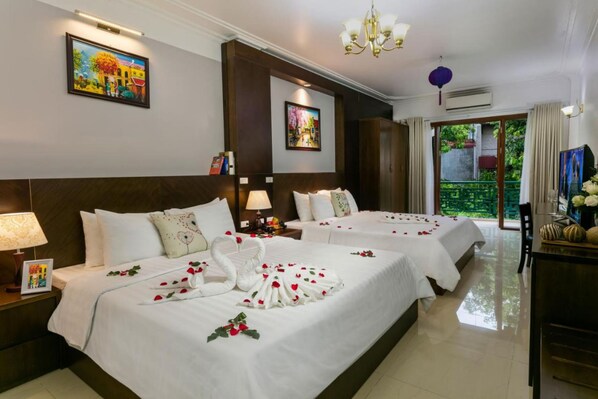 A hotel room with two beds, a chandelier, artwork on the walls, and a view of greenery outside.
